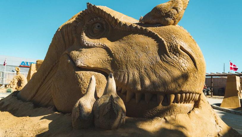 En dinosaur lavet i sand smiler i Hundested Sandskulptur Park