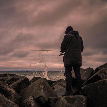 Mand står med ryggen til i blæsevejr og fisker i havet