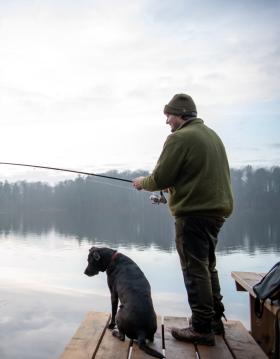 Mand og hund fisker ved en sø og kigger efter tang på en fiskekrog