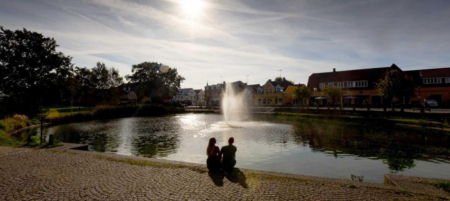 Et par sidder og kigger ud over Helsinge gadekær i aftensolen