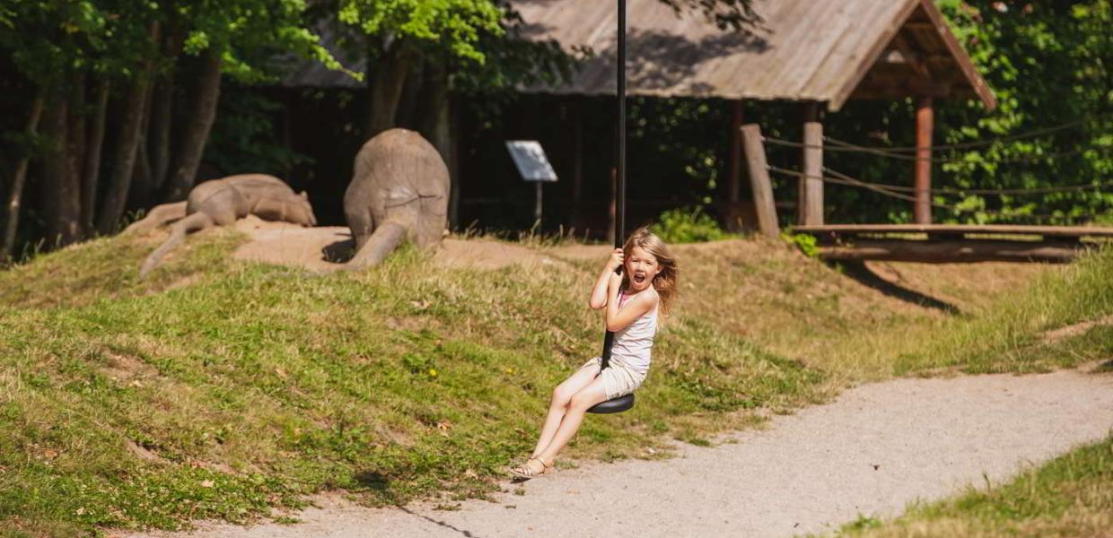 En pige ler, mens hun flyver afsted på svævebanen på Esrum Klosters naturlegeplads