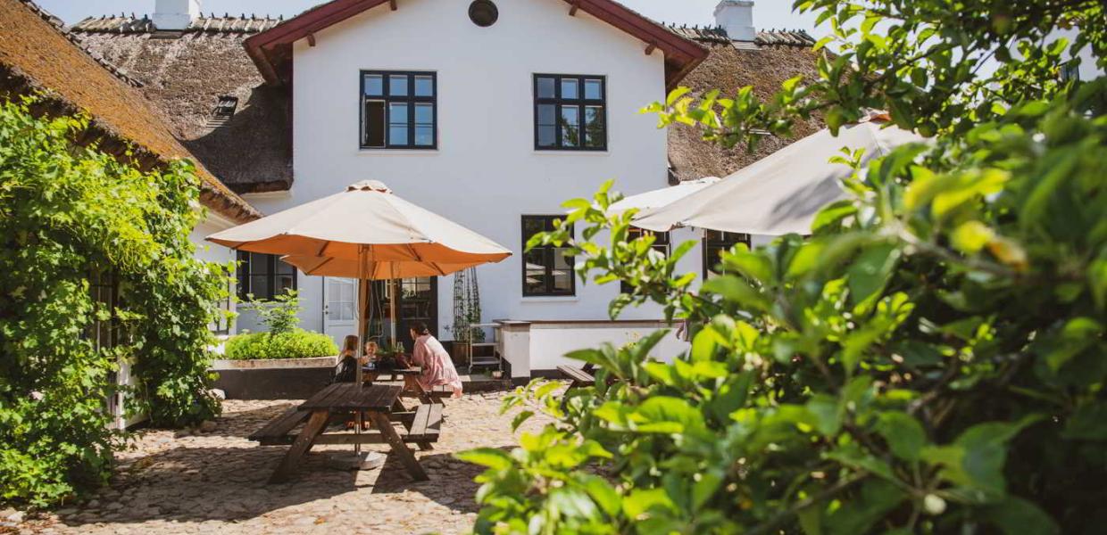 En mor og hendes børn spiser under en parasol i gårdhaven på Møllecaféen ved Esrum Kloster