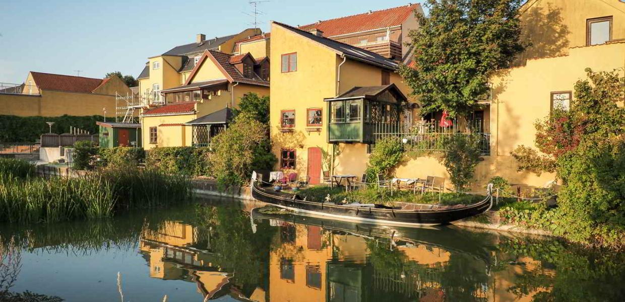 Hyggelige, gule bygninger ligger badet i solen på den anden side af kanalen i Frederiksværk