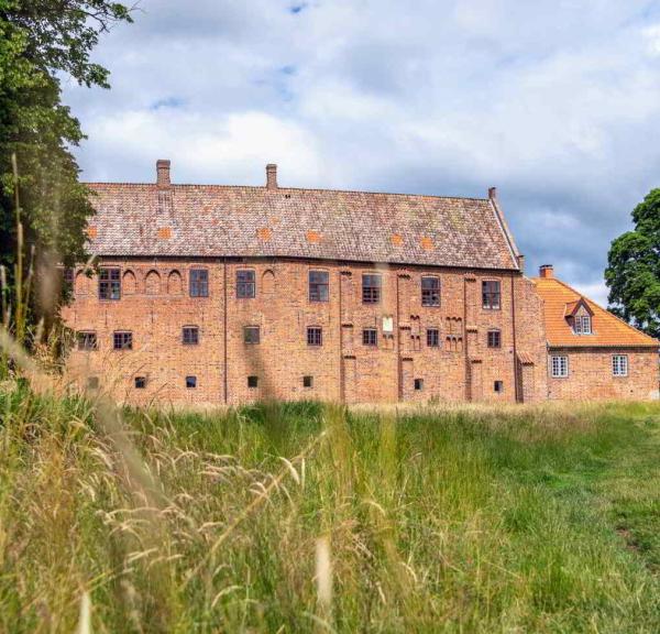 Esrum Klosters røde murstensbygning ligger for enden af en stor græsmark.