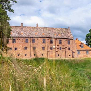 Esrum Klosters røde murstensbygning ligger for enden af en stor græsmark.